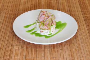 Üzerinde yeşil sos olan beyaz bir tabak. Tabak ahşap bir masaya konur.