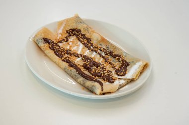 Çikolata soslu ve fındıklı bir tabak tatlı. Tabak beyaz ve üzerinde de tatlı var.