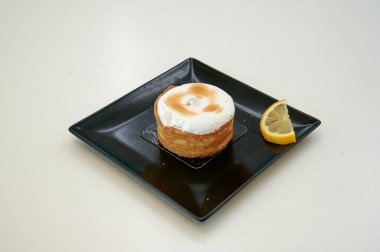 Üstünde limon dilimi olan küçük bir tatlı. Tatlı siyah bir tabakta.