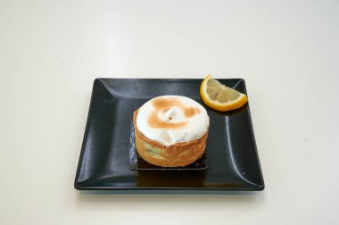 Üstünde limon dilimi olan küçük bir tatlı. Tatlı siyah bir tabakta.