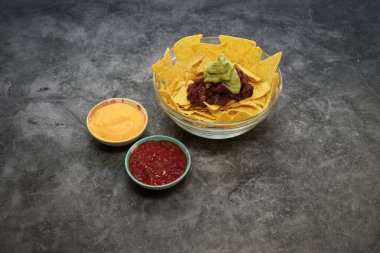 Guacamole ve salsa soslu bir kase nachos. İki kase salsa ve guacamole var.