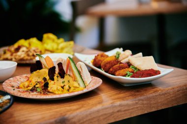 İki tabak yemeğin olduğu bir masa, biri salatalı, diğeri de sandviçli. Masada başka yemekler de var.