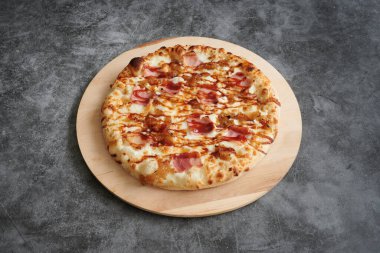 Tahtada jambonlu ve peynirli bir pizza. Pizza gri bir yüzeyde. Pizza dilimlenmiş.