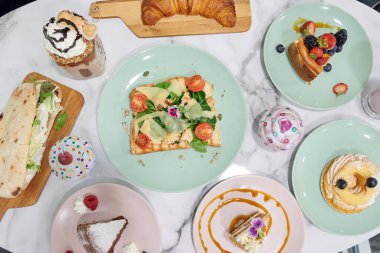 İçinde pasta, sandviç ve waffle da dahil olmak üzere bir sürü farklı yemek çeşidi olan bir masa.