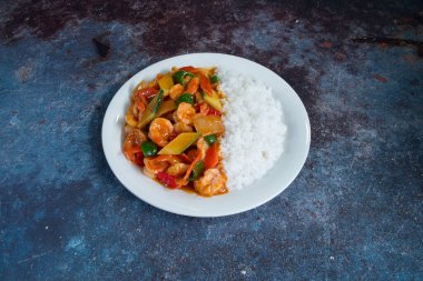 Pirinç ve sebzeli bir tabak yemek. Tabak beyaz, yemek kırmızı ve yeşil.