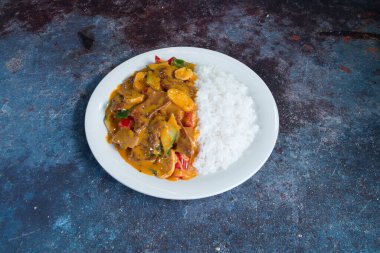 Pirinç ve etli bir tabak yemek. Pirinç beyaz ve et kırmızıdır. Tabak mavi bir yüzeyde.