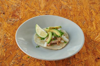 Beyaz tabakta avokado ve limonlu taco. Taco ahşap bir masanın üzerinde.