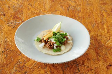 Üzerinde limon olan bir taco. Taco beyaz bir tabakta. Tabak ahşap bir masanın üzerinde.