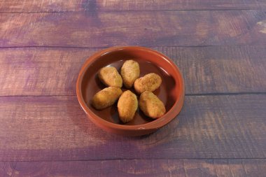 İçinde altı parça yiyecek olan bir kase kızarmış yiyecek. Kase kahverengidir ve seramiktir.