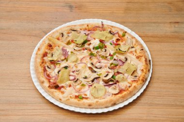 Beyaz tabakta mantarlı ve soğanlı bir pizza. Pizza ahşap bir masanın üzerinde. Pizza dilimlenmiş.