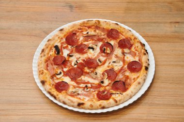 Beyaz tabakta pepperonili ve mantarlı pizza. Pizza ahşap bir masada oturuyor.