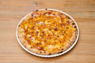 Tahta bir masada soğanlı ve peynirli bir pizza. Pizza beyaz bir tabakta. Pizza yuvarlak ve üzerinde bir sürü peynir var.