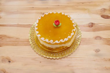 Üstünde gül olan sarı bir pasta. Tabağın üzerinde duruyor. Tabak ahşap bir masanın üzerinde.