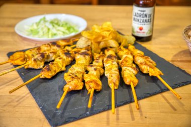 Masada bira şişesi olan bir tabak tavuk şişi. Şişede kırmızı beyaz bir logo var.