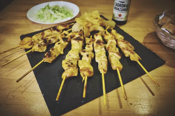 Masada bira şişesi olan bir tabak tavuk şişi. Şişede bir balığın resmi var.