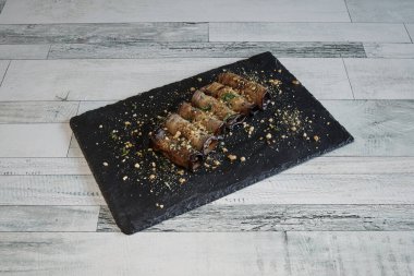 Siyah plakalı ve beyaz arka planı olan bir tabak yemek. Yemek hamura sarılmış bir tür yemektir.