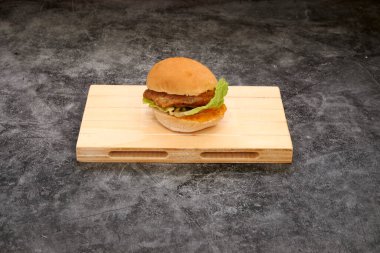 Üstünde taze marul olan lezzetli bir hamburger tahta bir kesme tahtasının üzerinde duruyor. Ekmek hafif kızarmış, et de mükemmel bir şekilde pişmiş. Marul güzel bir çıtır ekliyor.
