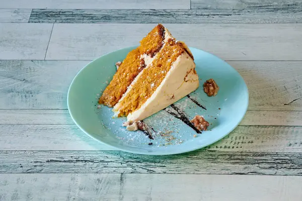 Mavi tabakta bir dilim havuçlu kek. Pasta fındıkla kaplı. Tabak ahşap bir masanın üzerinde.
