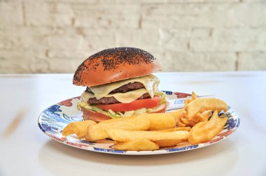 Peynirli bir hamburger ve ekmeğin üstüne domates. Yanında patates kızartması.