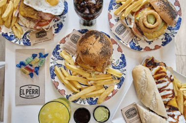 Dört tabak yiyecek ve içecekle dolu bir masa. Hamburger, patates kızartması ve sandviç de dahil.