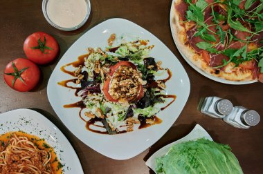 Üstünde domates olan bir tabak salata. Sağda bir pizza var. Sol tarafta bir kase salata var.