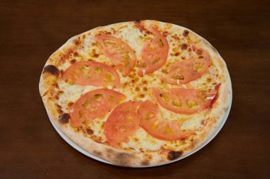 Üzerinde domates olan bir pizza. Pizza beyaz bir tabakta. Pizza ahşap bir masanın üzerinde.