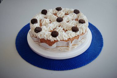 Üzerinde beyaz krema ve çikolata parçacıkları olan bir pasta. Pasta mavi bir masa örtüsünün üzerinde duruyor.