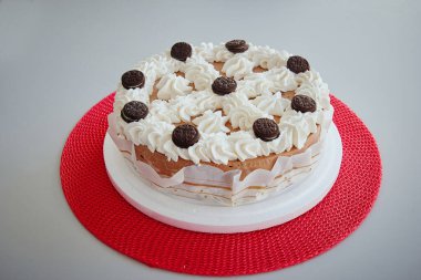 Üzerinde beyaz krema ve çikolata parçacıkları olan bir çikolatalı pasta. Pasta kırmızı bir bezin üzerinde duruyor.