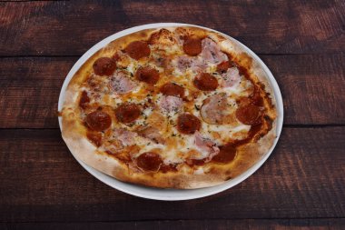 Ahşap bir masada pepperonili ve jambonlu pizza. Pizza beyaz tabakta.