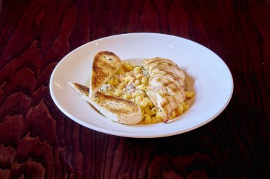 Tavuk, makarna ve ekmekten oluşan lezzetli bir yemek beyaz bir tabakta servis edilir. Ekmek tavuğun soluna konur ve makarna tabağa yayılır.