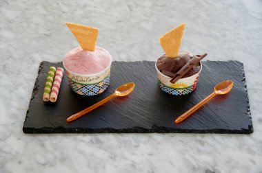 Üstünde gofret olan iki dondurma fincanı. Biri pembe ve diğeri çikolata. Masada iki kaşık var.