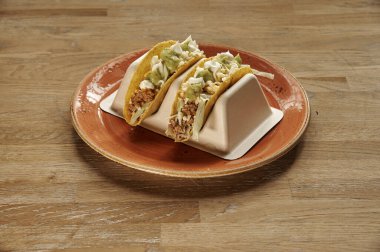 Bir tabakta iki taco. Biri solda ve diğeri de sağda. Tabak turuncu.