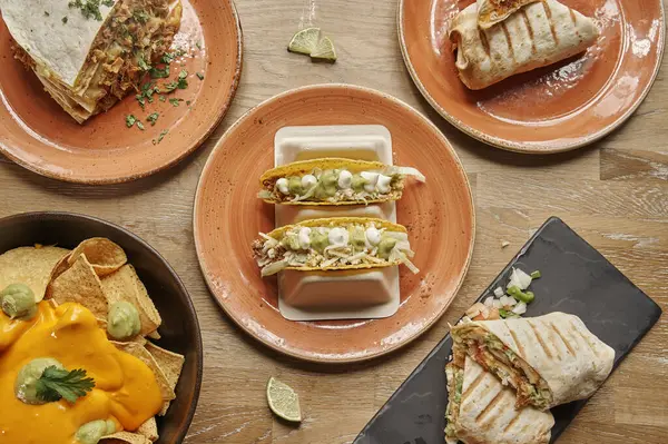 İçinde taco, burrito ve nachos bulunan dört tabak yemek olan bir masa. Tabaklar sıraya dizildi, takolar solda, dürümler ortada.