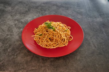 Üstünde maydanoz olan bir tabak spagetti. Tabak kırmızı ve spagetti uzun.