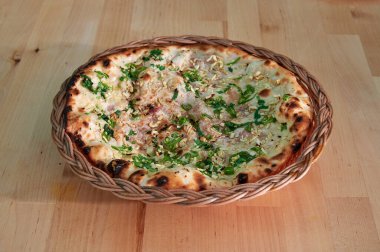 Otlu ve peynirli bir pizza ahşap bir masada oturur. Kabuğu kahverengi, peyniri erimiş.