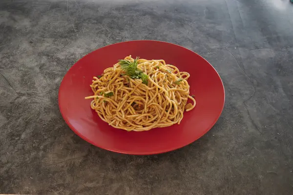 Üstünde maydanoz olan bir tabak spagetti. Tabak kırmızı ve spagetti uzun.