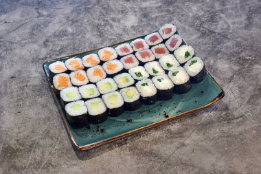 Bir tabak çeşit suşi rulosu. Ekmekler farklı renkte ve tatlarda. Tabak tezgahın üstünde.