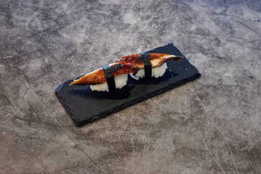 Üzerinde siyah bambu çubuğu olan bir suşi rulosu. Suşi rulosu siyah bir tabakta duruyor.