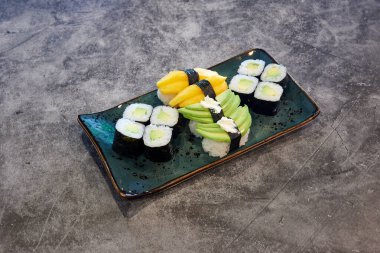 Avokado ve salatalıklı bir tabak suşi. Plakası mavi ve siyah bir kenarı var.