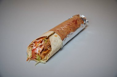 Marul ve etle birlikte bir paket yiyecek. Folyoya sarılmış. Beyaz bir yüzeyde duruyor.