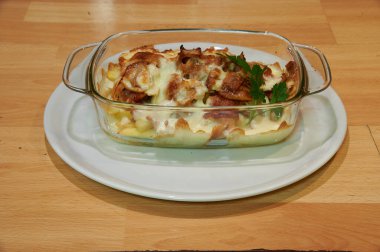 Üzerinde bir tabak yemek olan beyaz bir tabak. Yemek, peynirli ve etli bir güveç.