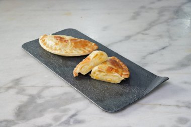 Siyah tepside iki hamur işi. Biri açık. Diğeri ise kapalı. Tepsi mermer tezgahın üzerinde.