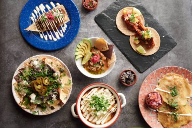 Bir masa taco, burrito ve enchilada gibi çeşitli Meksika yemekleri ile doludur. Birkaç kase ve farklı yemek çeşitleri var, bazıları guacamole ile birlikte.