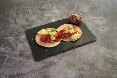 İki tane limonlu taco. Biri kırmızı ve diğeri sarı. Tacoların yanında bir kase sos var.