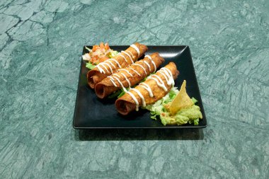 Yanında guacamole ve marul olan bir tabak tortilla. Tortillalar beyaz sosla kaplı.