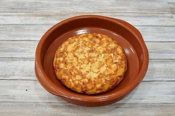 Tahta bir masanın üzerinde bir tabak yemek duruyor. Tabak yuvarlak, altın rengi kahverengi yiyeceklerle dolu.