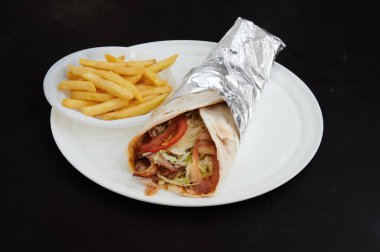 Marul ve domatesli bir paket beyaz bir tabakta patates kızartmasının yanında duruyor. Paket folyoya sarılmış.