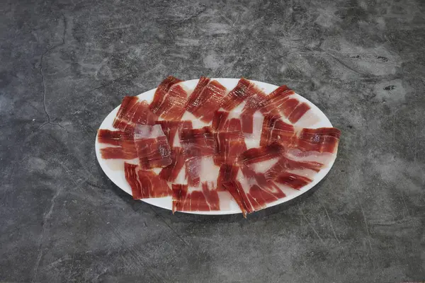 Üzerinde çeşit çeşit kesilmiş et olan beyaz bir tabak. Et dairesel bir düzende, bazı parçalar birbiri ile örtüşüyor. Tabak gri bir yüzeye yerleştirilmiş.