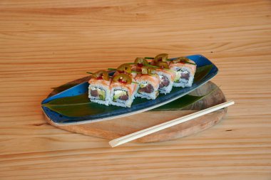 Üstünde yeşil yaprak olan bir tabak suşi. Suşi dört parçaya bölündü. Tabakta iki çubuk var.