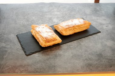 Siyah tabakta iki hamur işi. Bir tanesi pudra şekeriyle kaplı. Diğeri değil.